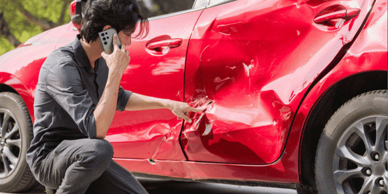 Man on the phone checking his red car with a large dent on the side