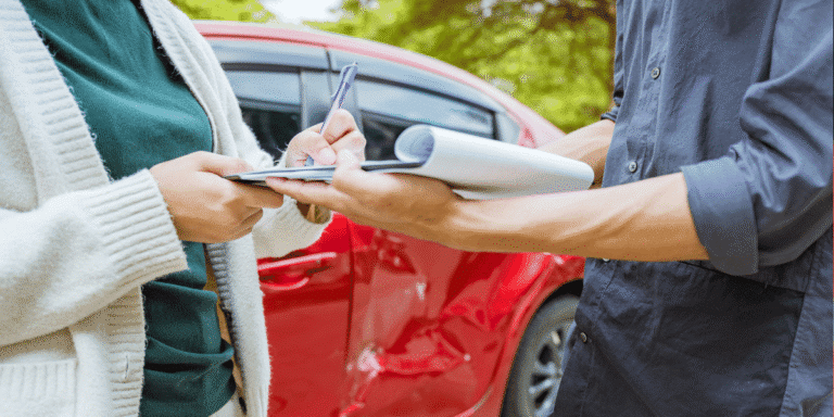 Close up of two individuals signing paperwork with a car accident in the background