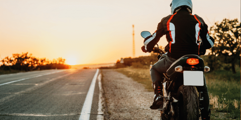 Back shot of a motorcyclist driving on a road with the sunset in front of him