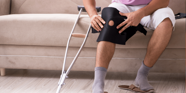 Close up of an individual adjusting their knee brace with crutches next to them